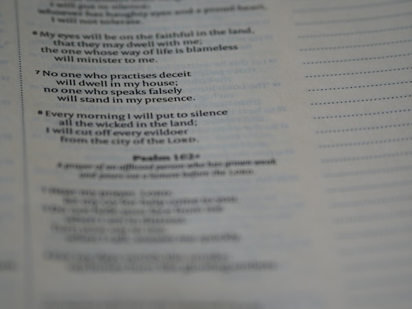 The image contains a close-up shot of a page from a book with text clearly focused in the center and blurred towards the edges. The text appears to be religious or scriptural, with numbered verses and phrases referencing moral conduct.