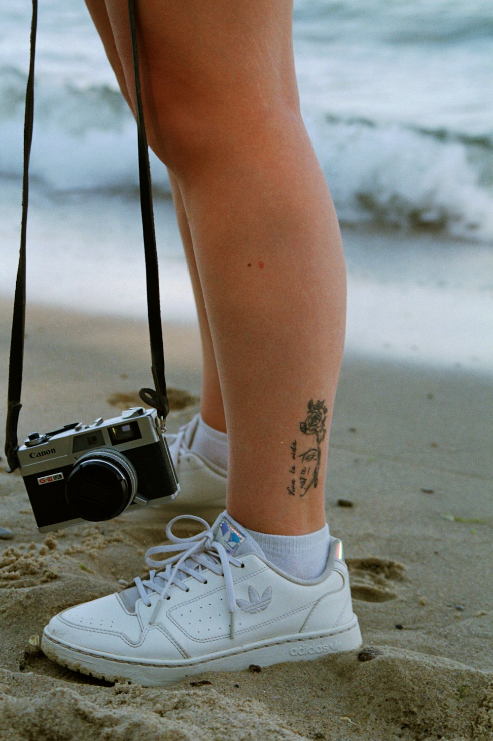 a person's legs with a camera on a beach
