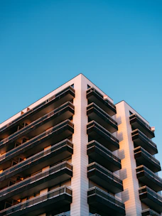 A sleek, modern high-rise apartment building with glass balconies overlooking the Dubai skyline at sunset.