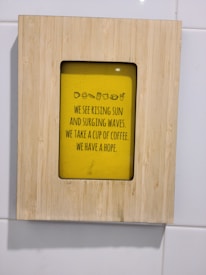 A wooden frame surrounds a yellow poster with a motivational message about hope and coffee. The text includes small icons of a cup and other food items.