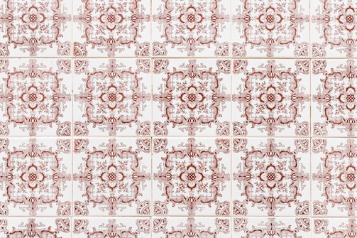 A repeating pattern of ornate, vintage-style ceramic tiles with intricate designs in a red-brown color, arranged in a grid formation on a white background.