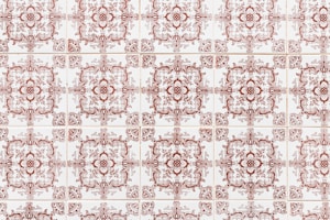 A repeating pattern of ornate, vintage-style ceramic tiles with intricate designs in a red-brown color, arranged in a grid formation on a white background.