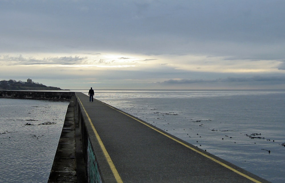 a person walking on a road next to a body of water