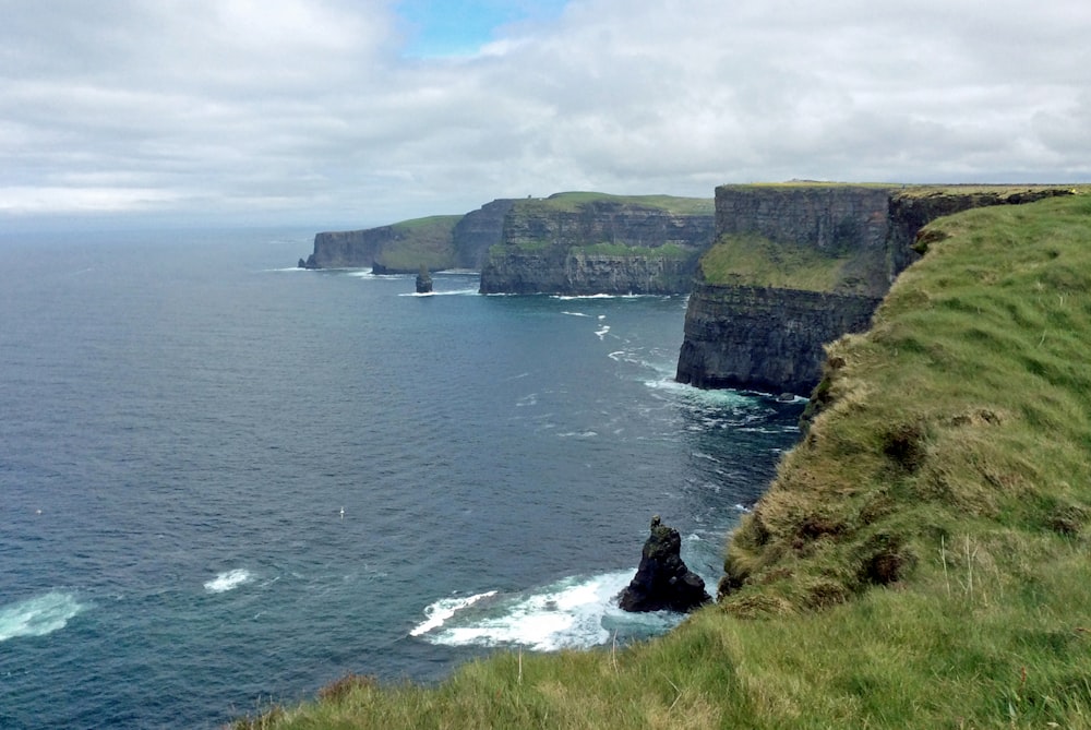 a cliff side with a body of water below with Cliffs of Moher in the background