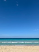 A serene beach with turquoise waves gently lapping the shore under a clear blue sky.