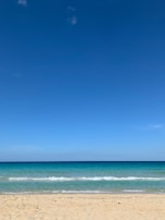 A peaceful beach scene with turquoise waves gently lapping the shore under a clear blue sky.