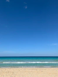 A serene tropical beach with turquoise waves gently lapping the white sand under a bright blue sky.