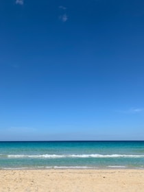 A serene tropical beach with turquoise waves gently lapping white sand under a sunny sky.