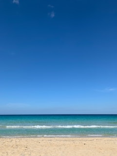A serene beach scene with turquoise waves gently lapping white sand under a clear blue sky.