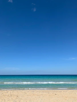 A serene tropical beach with turquoise waves gently lapping the white sand under a bright blue sky.