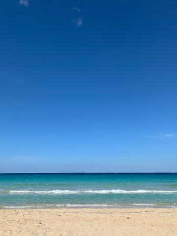 A serene beach scene with turquoise waves gently lapping white sand under a clear blue sky.