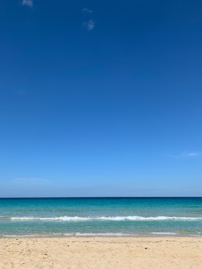 A sunlit beach with turquoise waves gently lapping the shore under a clear blue sky.