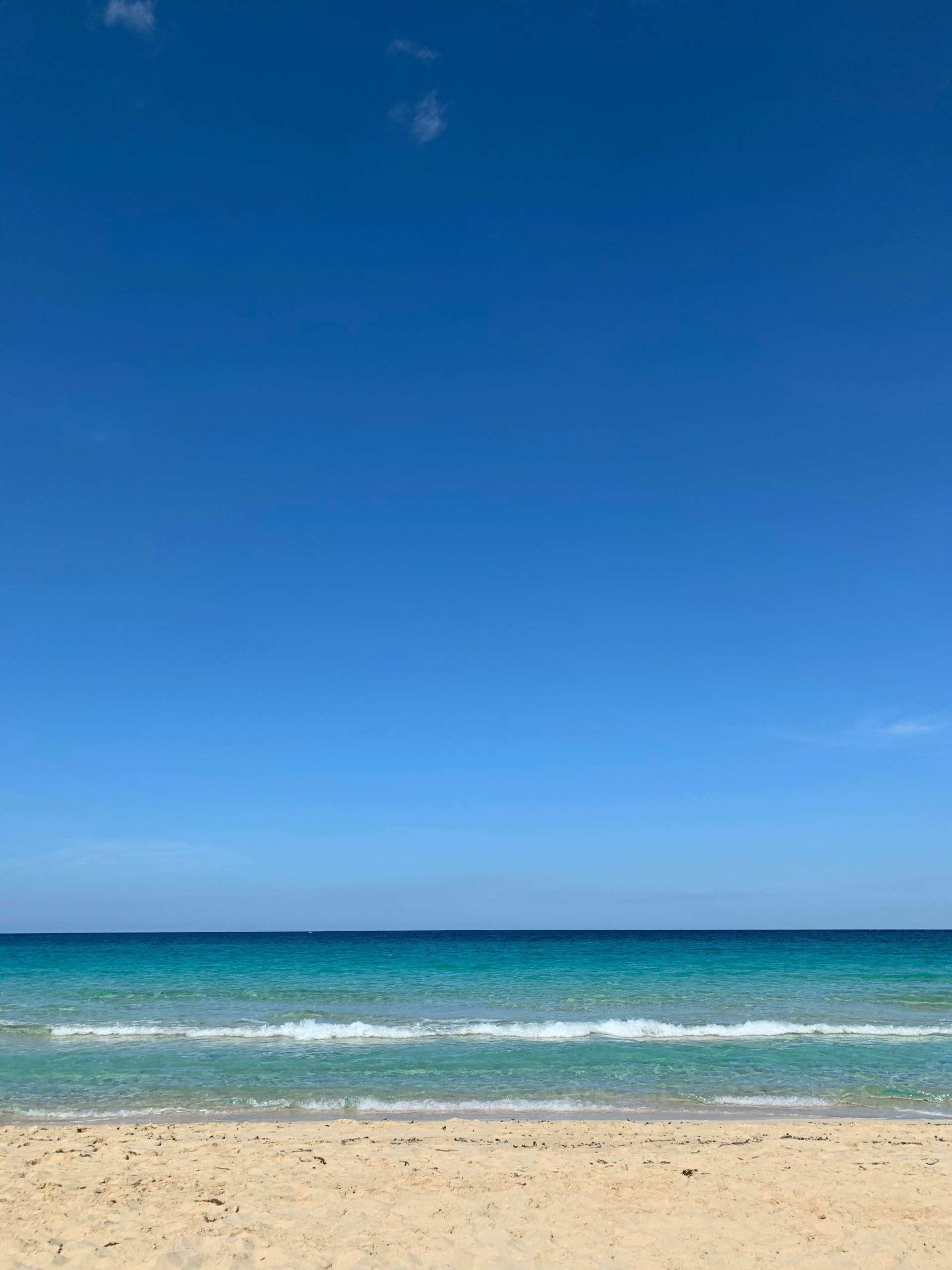 A serene beach view with turquoise waves gently rolling onto white sand under a clear blue sky.