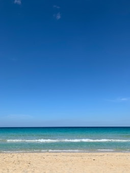 A serene beach scene with clear blue skies, turquoise ocean waves gently lapping against a sandy shore.