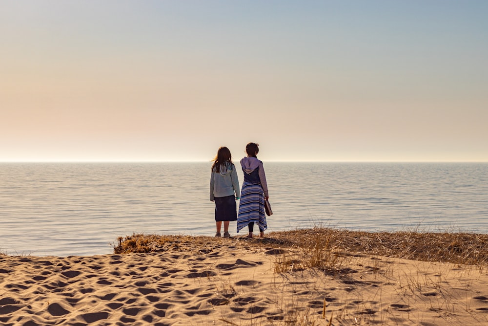 a man and woman standing on a beach looking at the water