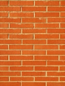 A wall constructed from red bricks, each uniformly sized and horizontally arranged in staggered rows with beige mortar filling the gaps between the bricks. The surface appears textured and the color is a vivid, warm red.