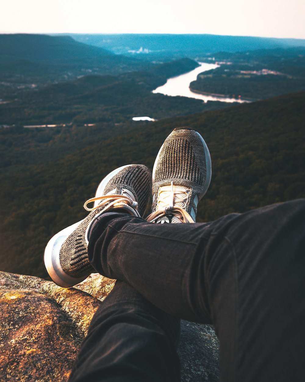 os pés de uma pessoa em uma rocha com vista para um rio e montanhas