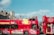 A brightly colored red double-decker bus with 'City Sightseeing Bath' written on the side. The bus features various vibrant designs, including the Union Jack and iconic city landmarks. People are seated on the upper open-top deck, enjoying the view of historical buildings and a clear sky.