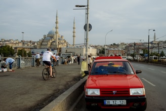 a red car on a road with people and a building in the background