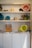 Shelves filled with various colored buckets, rustic tools, and plant pots. The bottom section features a wooden box holding magazines and a stack of papers next to more buckets.
