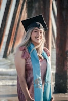 A graduation portrait with warm tones, featuring a smiling graduate holding their cap against a backdrop of ocean waves.