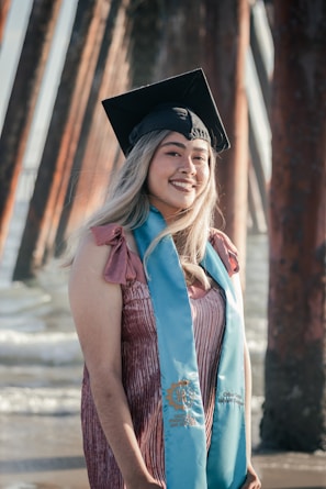 A graduation portrait with warm tones, featuring a smiling graduate holding their cap against a backdrop of ocean waves.