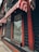 A building facade featuring striped red and white awnings over large windows. The structure has dark wood paneling with accents of red trim. Each window has an empty wooden planter box affixed beneath it. The street can be faintly seen reflected in the windows.