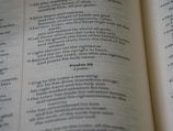 A close-up of an open Bible showing text from the Psalms with verses and numbers visible. The text is in a serif font and is printed on thin, slightly yellowed paper typical of a Bible.