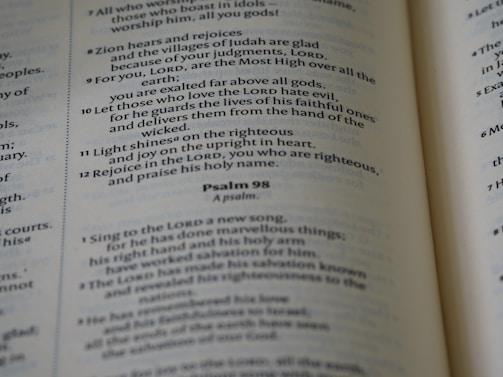 A close-up of an open Bible showing text from the Psalms with verses and numbers visible. The text is in a serif font and is printed on thin, slightly yellowed paper typical of a Bible.