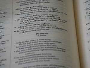 A close-up of an open Bible showing text from the Psalms with verses and numbers visible. The text is in a serif font and is printed on thin, slightly yellowed paper typical of a Bible.