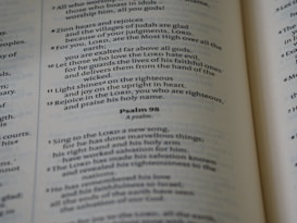 A close-up of an open Bible showing text from the Psalms with verses and numbers visible. The text is in a serif font and is printed on thin, slightly yellowed paper typical of a Bible.