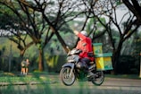 A delivery rider on a bike wearing a bright red jacket, speeding through city streets with a pizza box in hand.