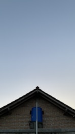A triangular brick house roof with a blue water tank installed at its top-center against a clear sky backdrop.