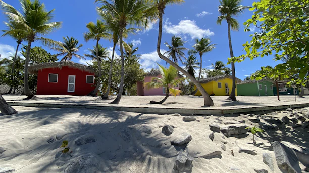 Colorful wooden houses lining a sandy street in Mano Juan village on Saona Island under a bright blue sky.