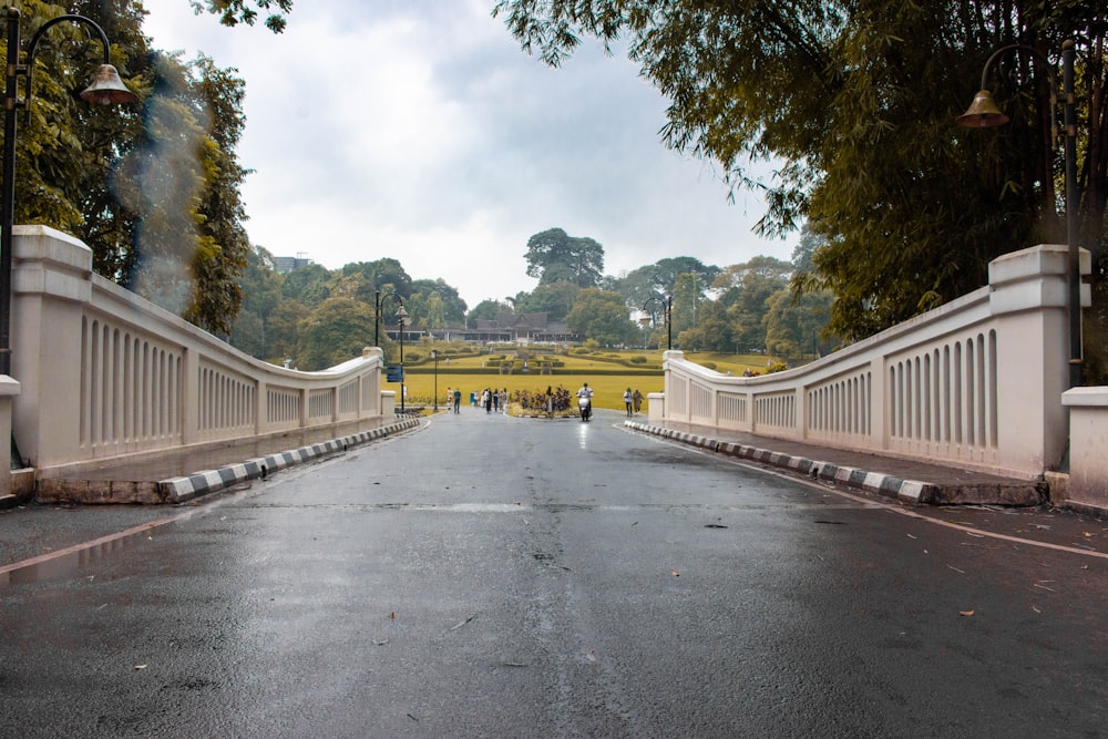 a road with a row of white fences and a row of people walking on the side