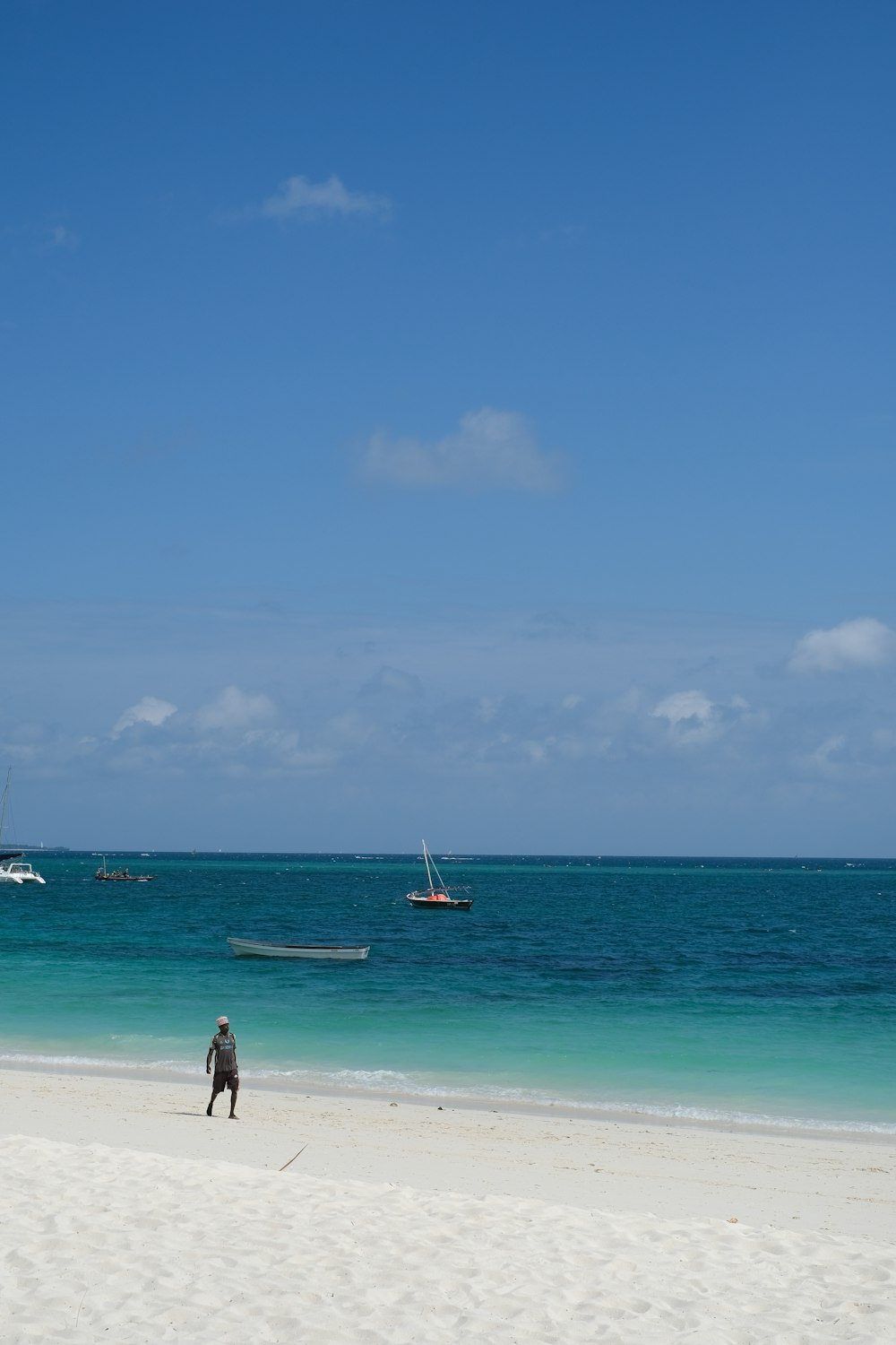 a person standing on a beach looking at a boat in the water