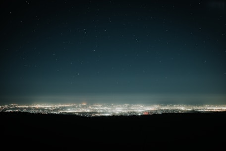 A futuristic cityscape illuminated with neon lights under a vast night sky filled with stars.
