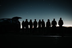 a group of people standing in front of a car at night
