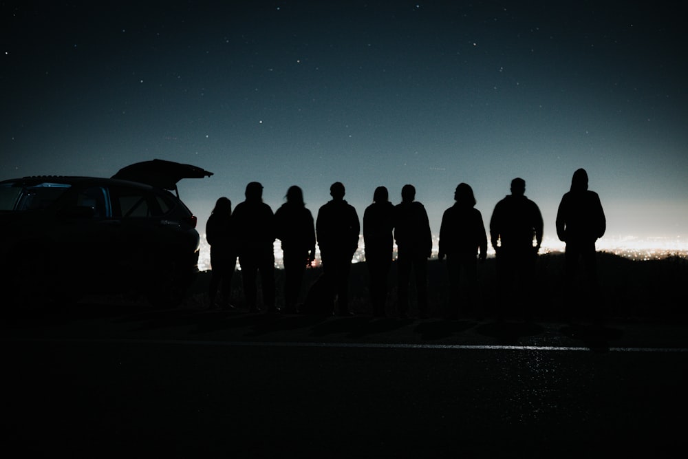 a group of people standing in front of a car at night