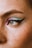 A close-up of the left eye area with detailed makeup featuring a blend of pastel blue and pink eyeshadow, accentuated by a bold black winged eyeliner. The skin is fair with visible freckles, and there is a small nose piercing on the side.
