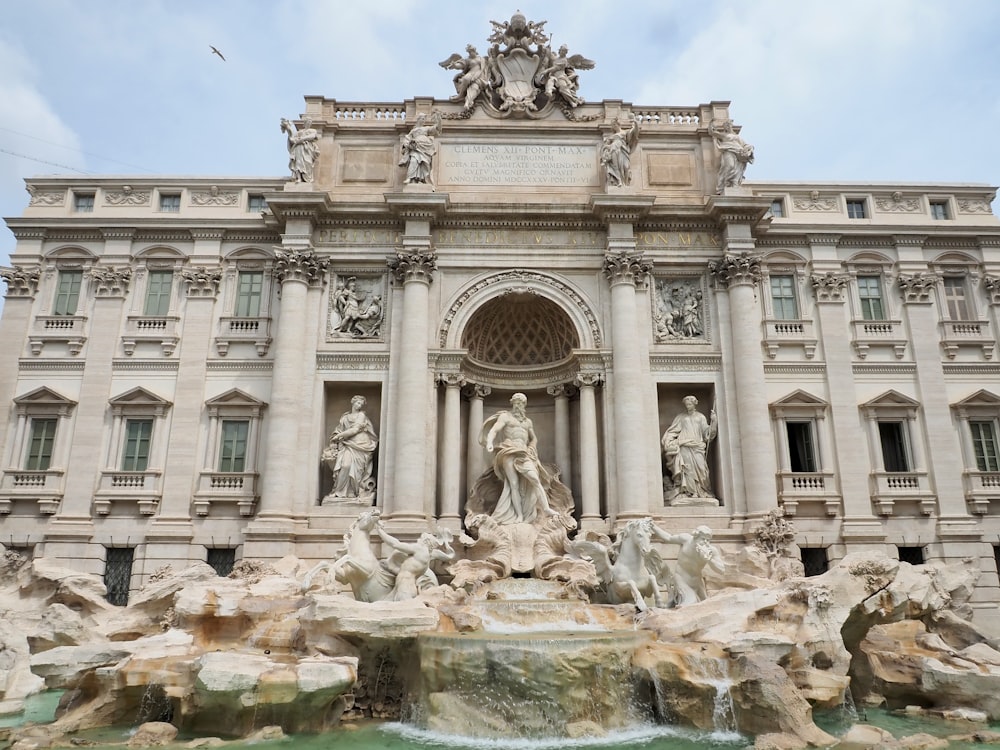 un gran edificio con estatuas y una fuente frente a él con la Fontana de Trevi al fondo