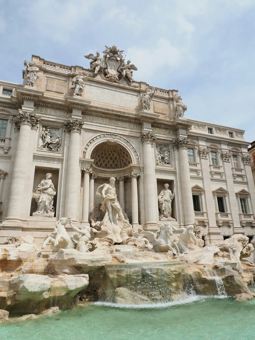 un gran edificio con estatuas y una fuente frente a él con la Fontana de Trevi al fondo