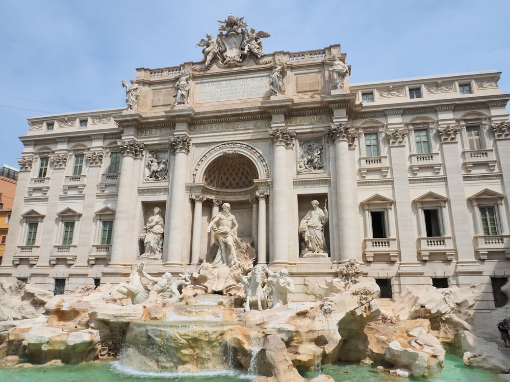 un gran edificio con estatuas y una fuente frente a él con la Fontana de Trevi al fondo