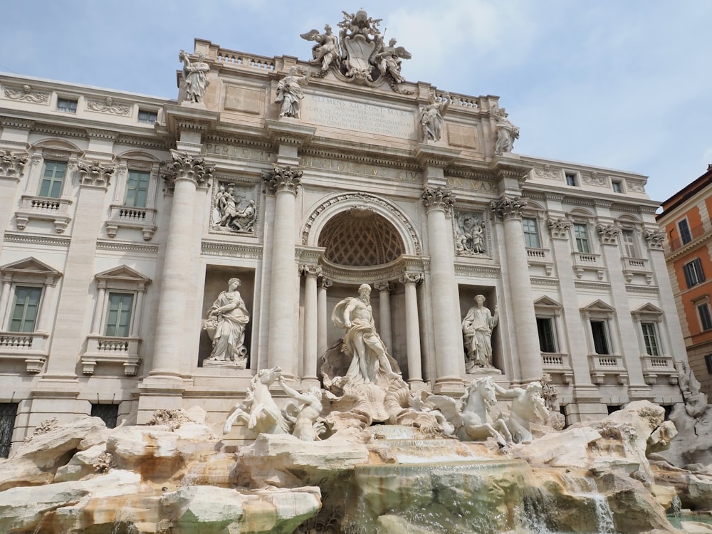 un gran edificio con estatuas frente a él con la Fontana de Trevi al fondo