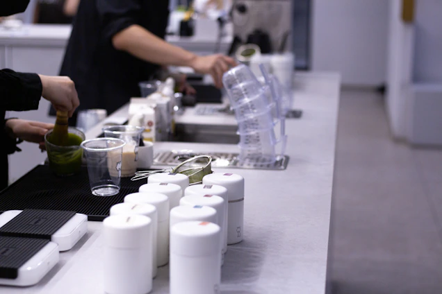 Close-up of hands preparing fresh ingredients beside a sleek blender and coffee machine on a clean kitchen counter.