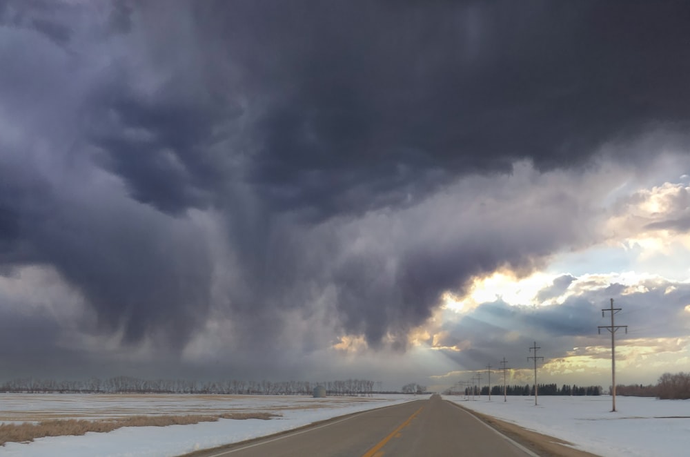 a road with snow on the side and a cloudy sky above