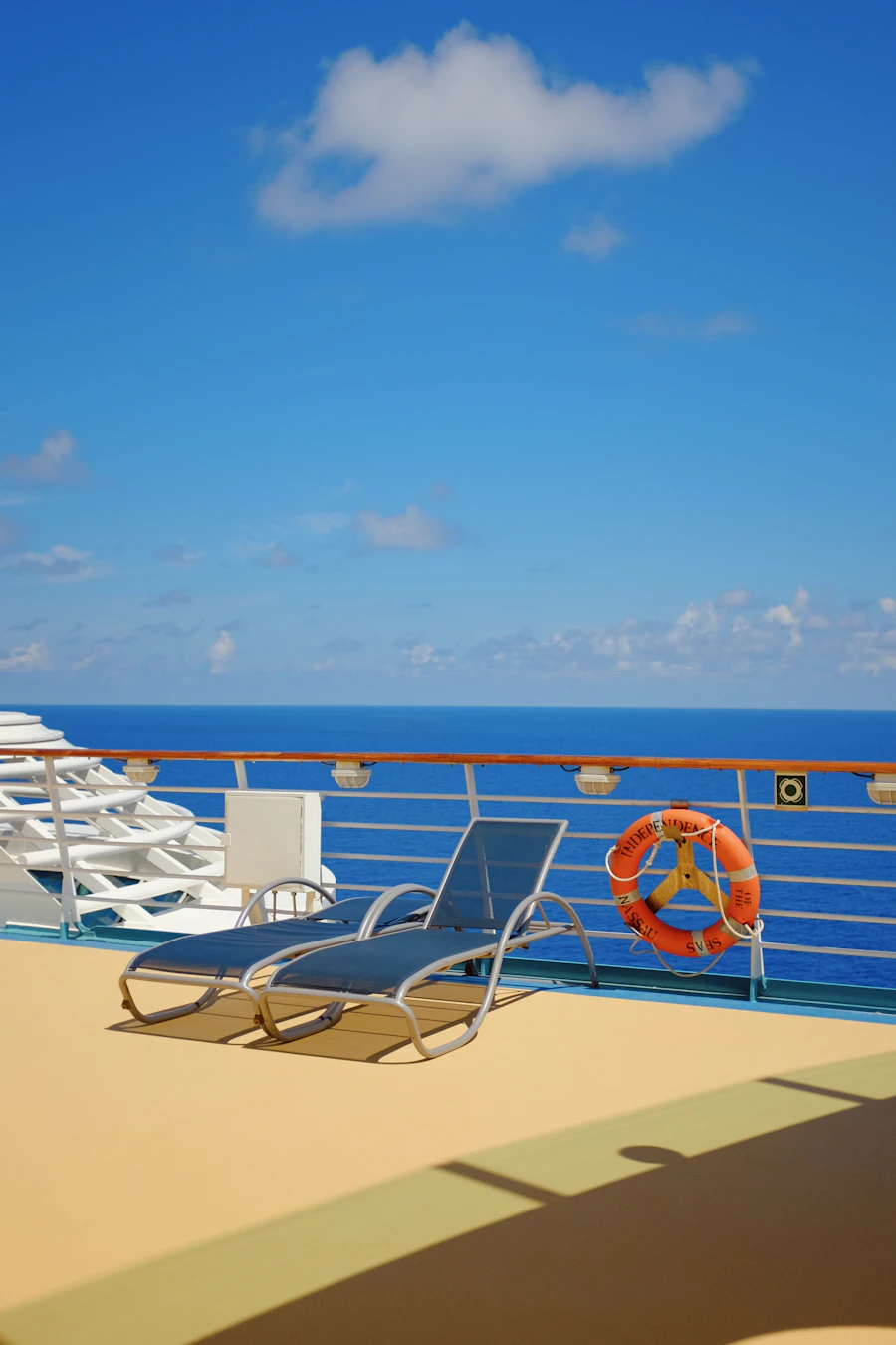 Cruise ship deck lounger beside a railing and life ring above deep blue sea