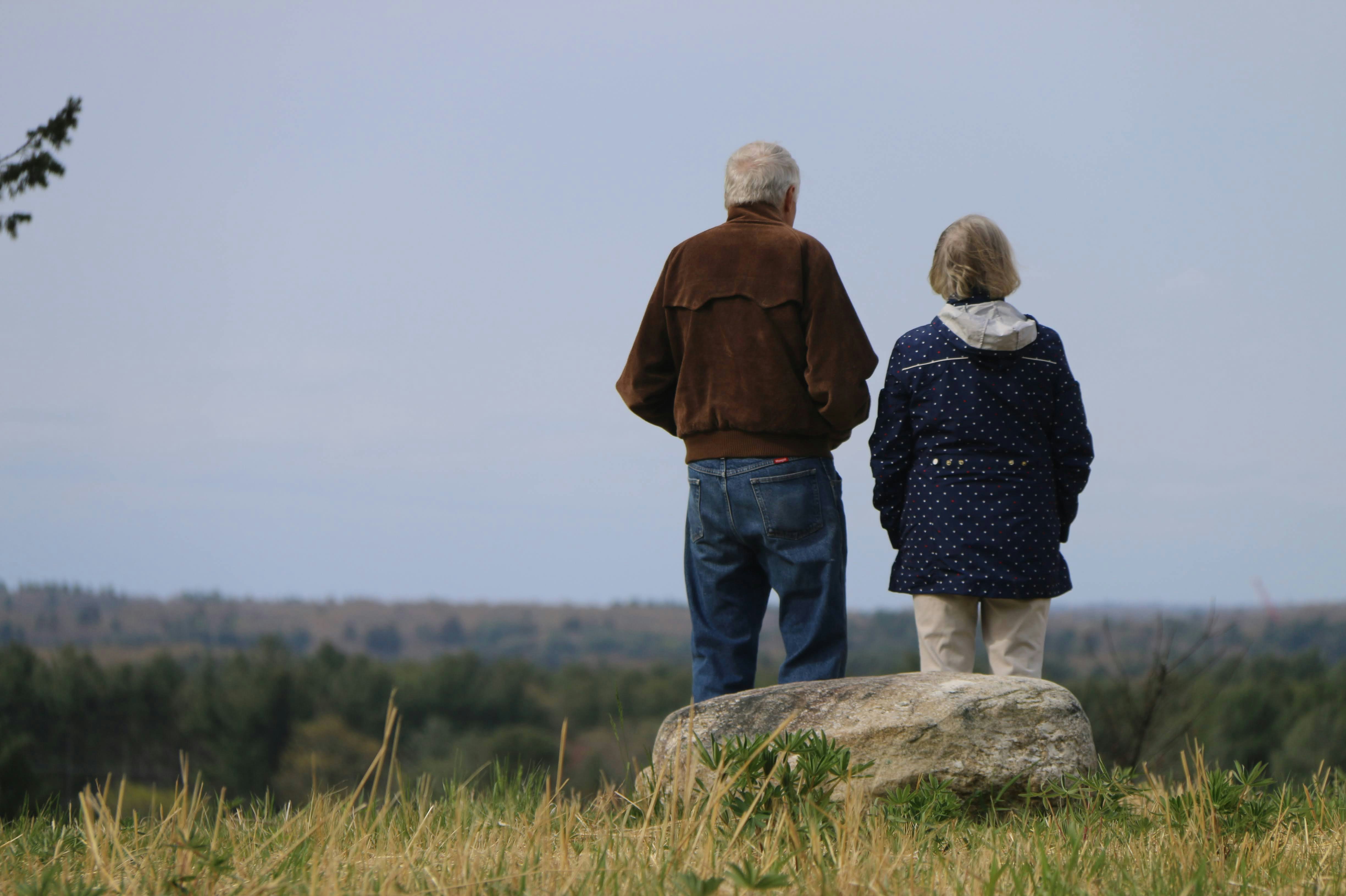 a man and woman standing on a rock overlooking a forest