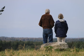 a man and woman standing on a rock overlooking a forest