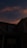 Dark silhouette of a house in the foreground with the evening sky lit in hues of orange and blue. A crescent moon is visible in the sky, surrounded by softly illuminated clouds.